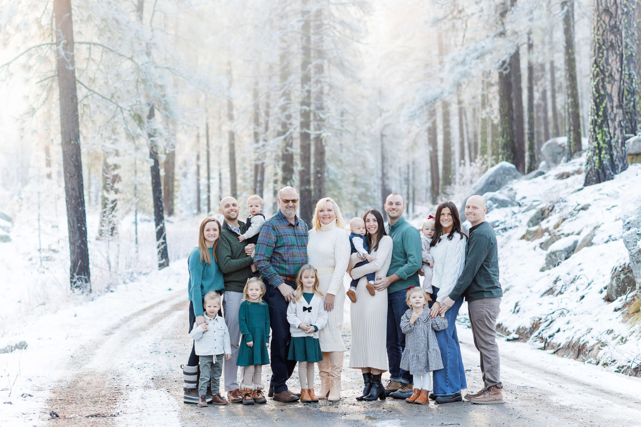 A large extended family stands in a forest road covered in snow smiling after visiting the Leavenworth Reindeer Farm