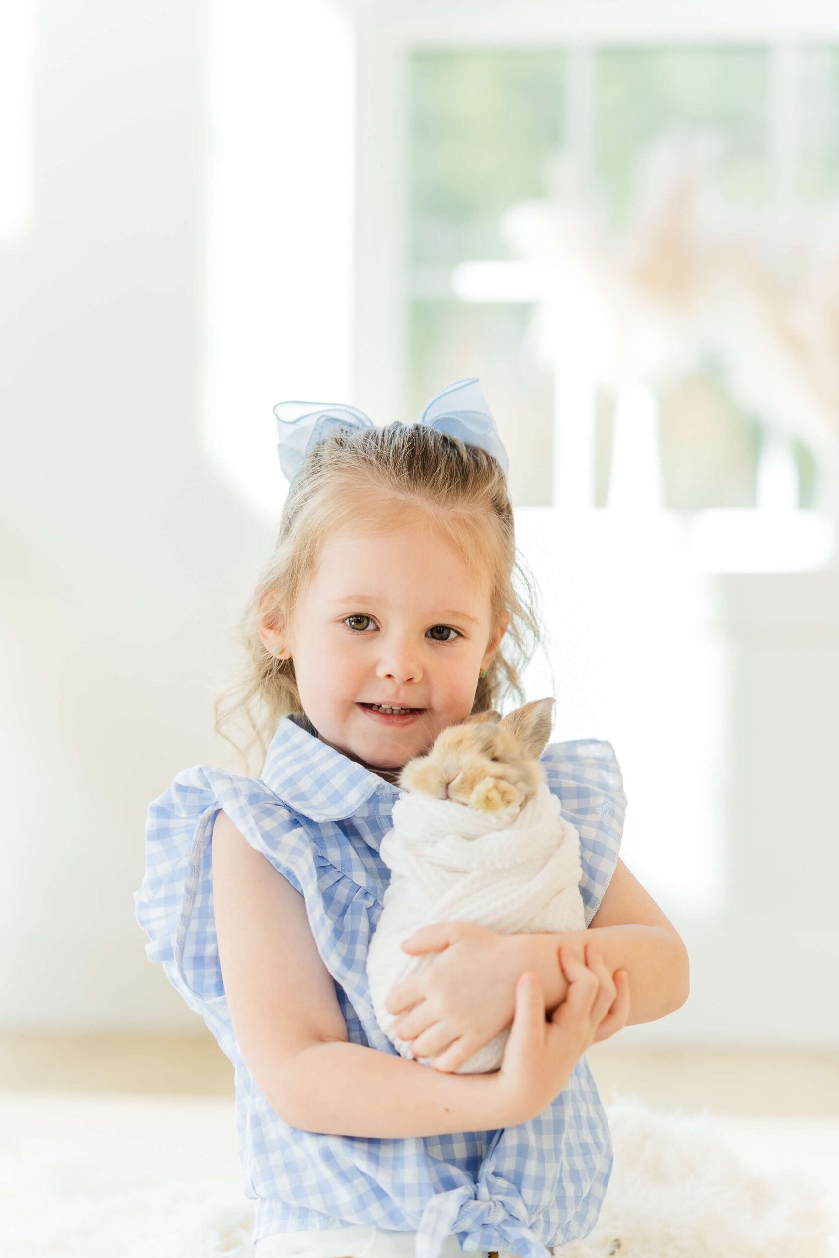 A toddler girl in blue dress hugs a swaddled baby bunny after visiting daycares in wenatchee