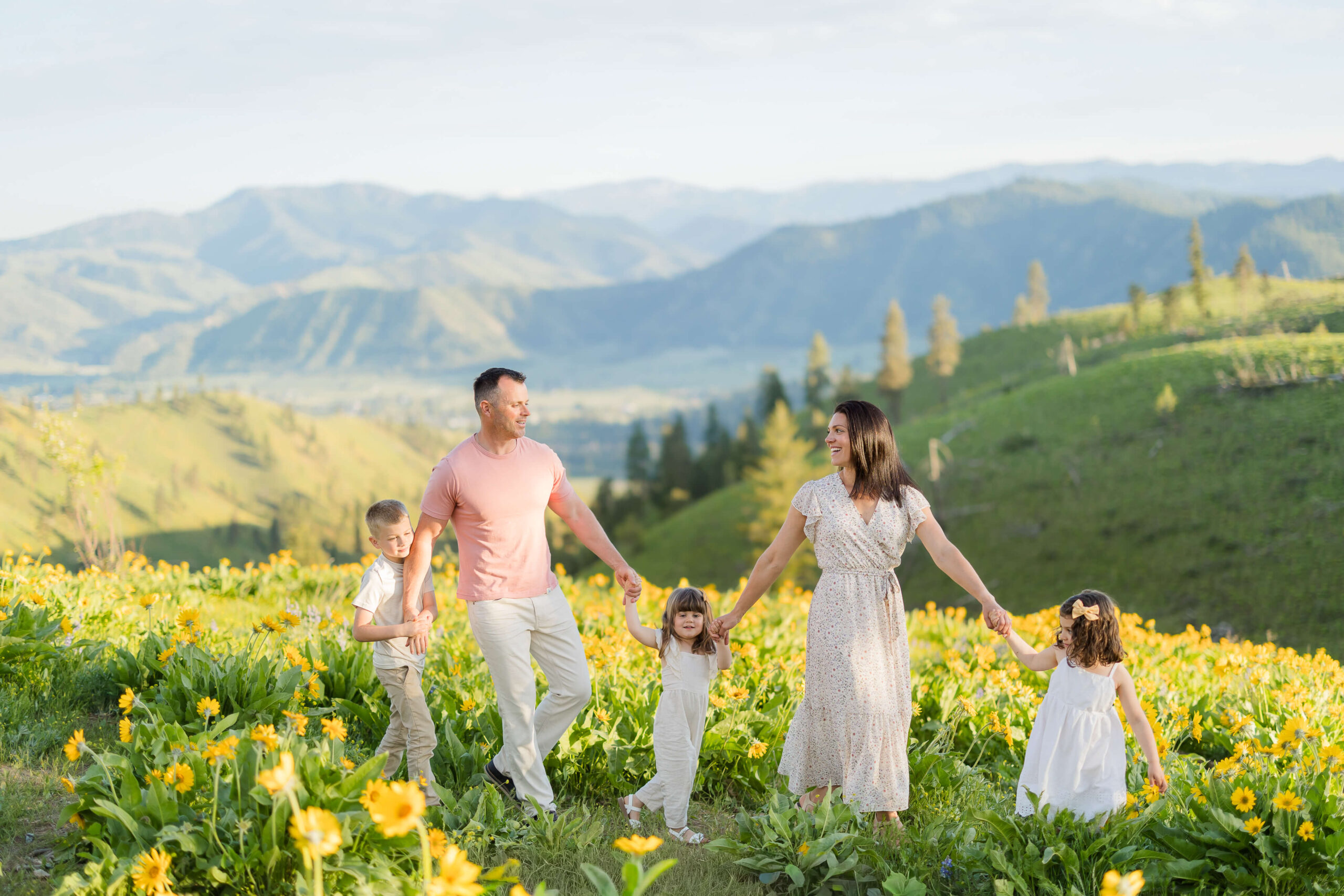 A mom and dad walk in a hill covered in yellow wildflowers at sunset holding hands with three young children while staying at family friendly hotels in leavenworth wa