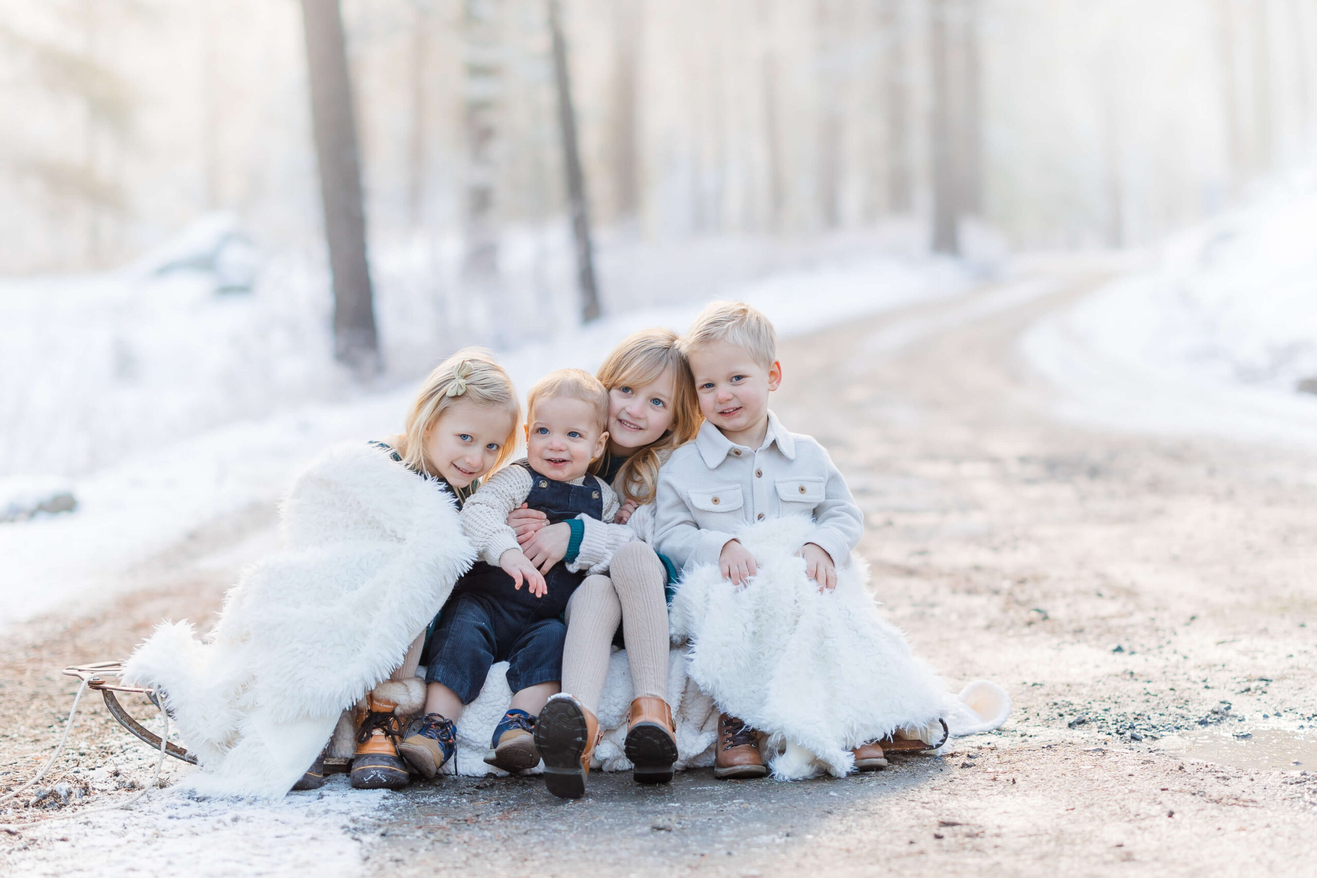 Found young brothers and sisters sit on a sled in a gravel road in a snowy forest in white outfits after visiting kid-friendly restaurants in Leavenworth, WA
