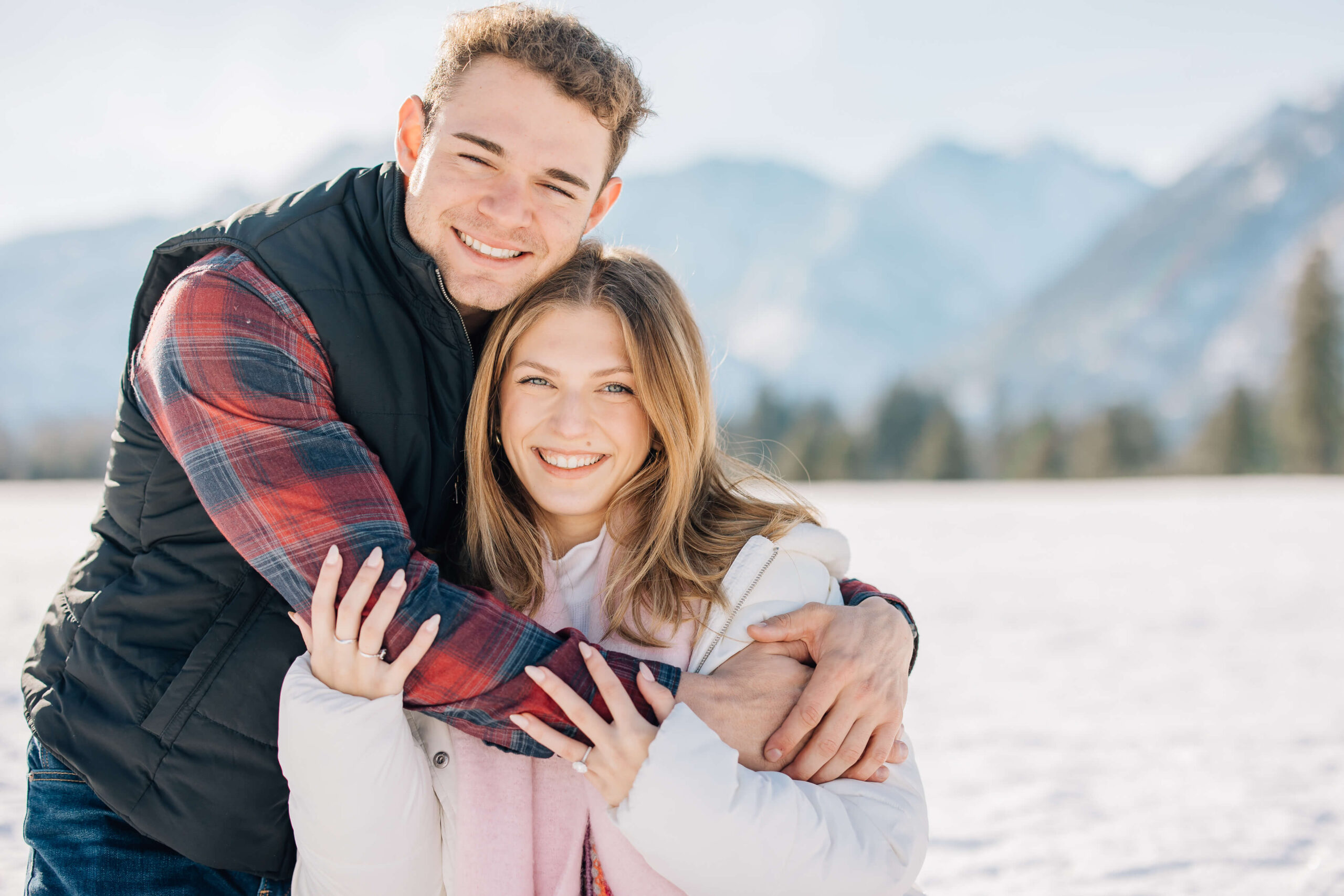 A happy couple in black and pink snuggle and hug in a snowy meadow after their leavenworth proposal