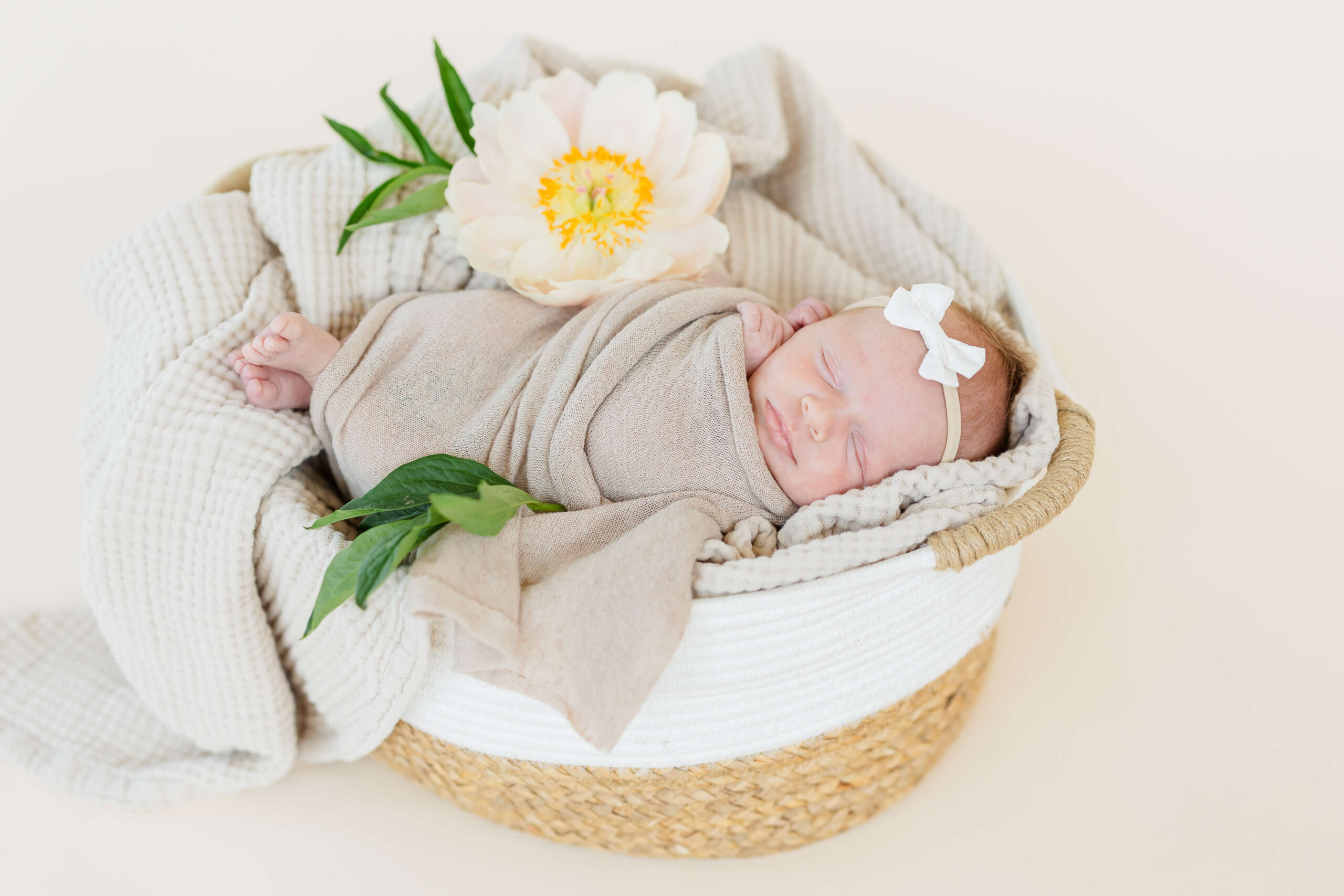 A sleeping newborn baby girl in a woven basket on a bed of blankets
