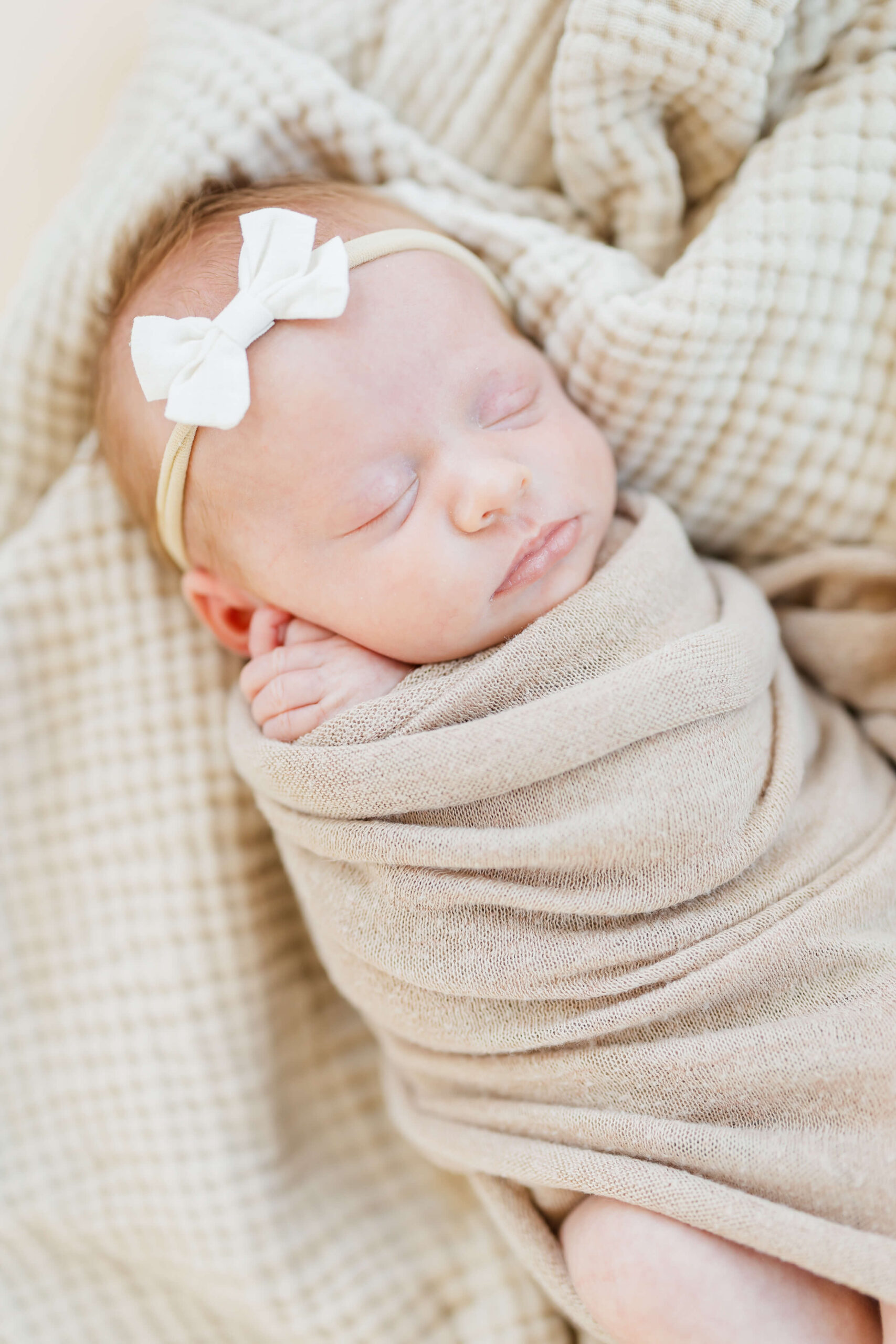 A baby girl in tan swaddle and white bow sleeps on a blanket after meeting pediatricians in wenatchee