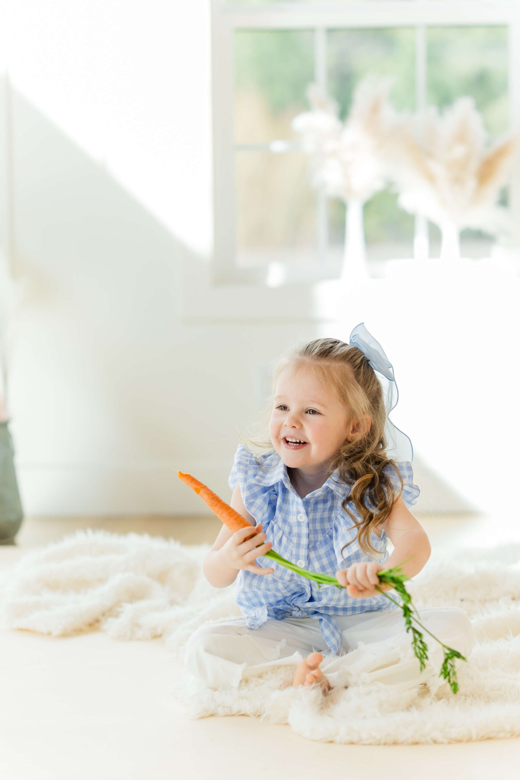 A happy young girl in a blue blouse holds a carrot while sitting on the floor of a studio after visiting playgrounds in leavenworth, wa