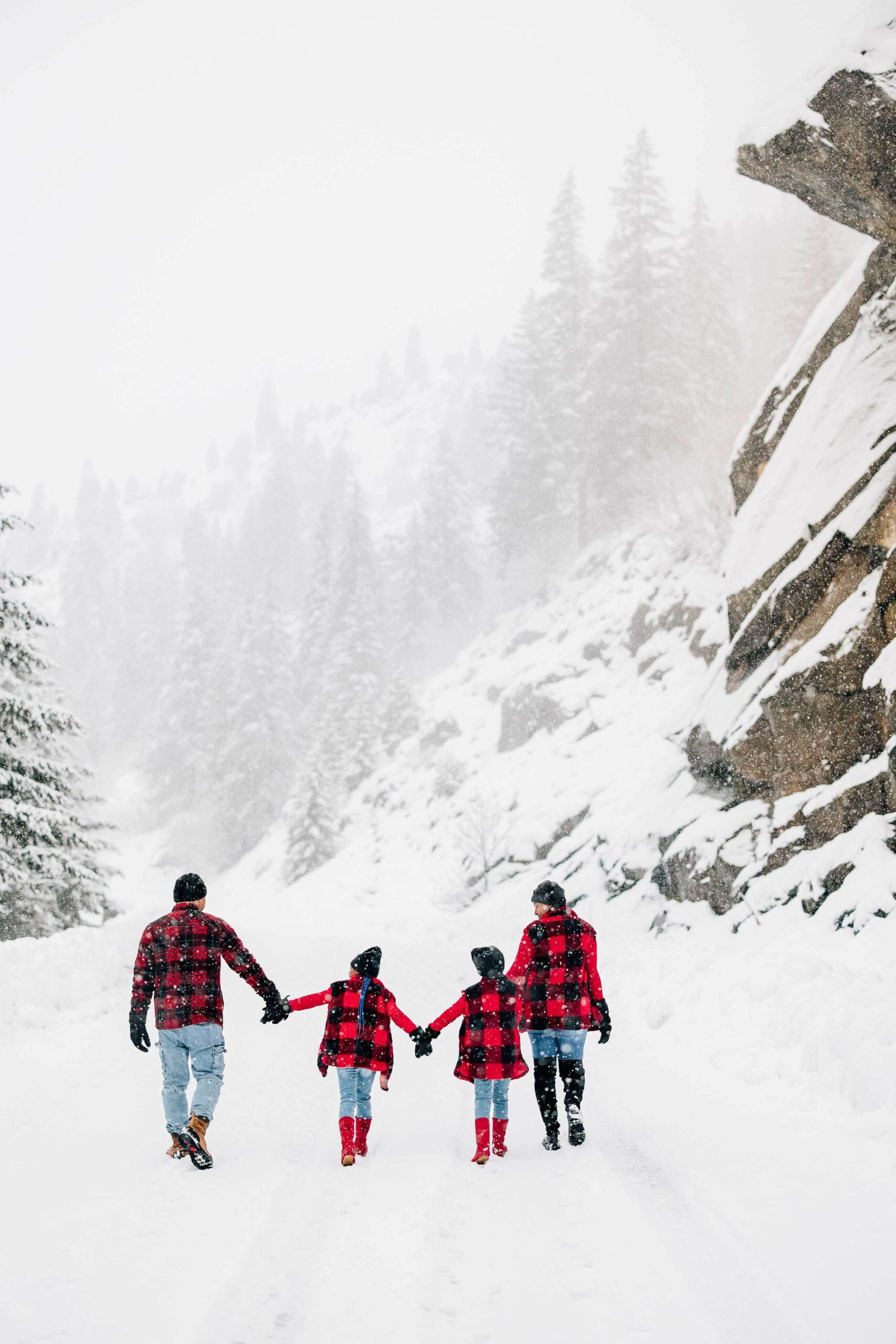 A happy family of four with two children walk a snow covered trail in the mountains holding hands during things to do in leavenworth with kids