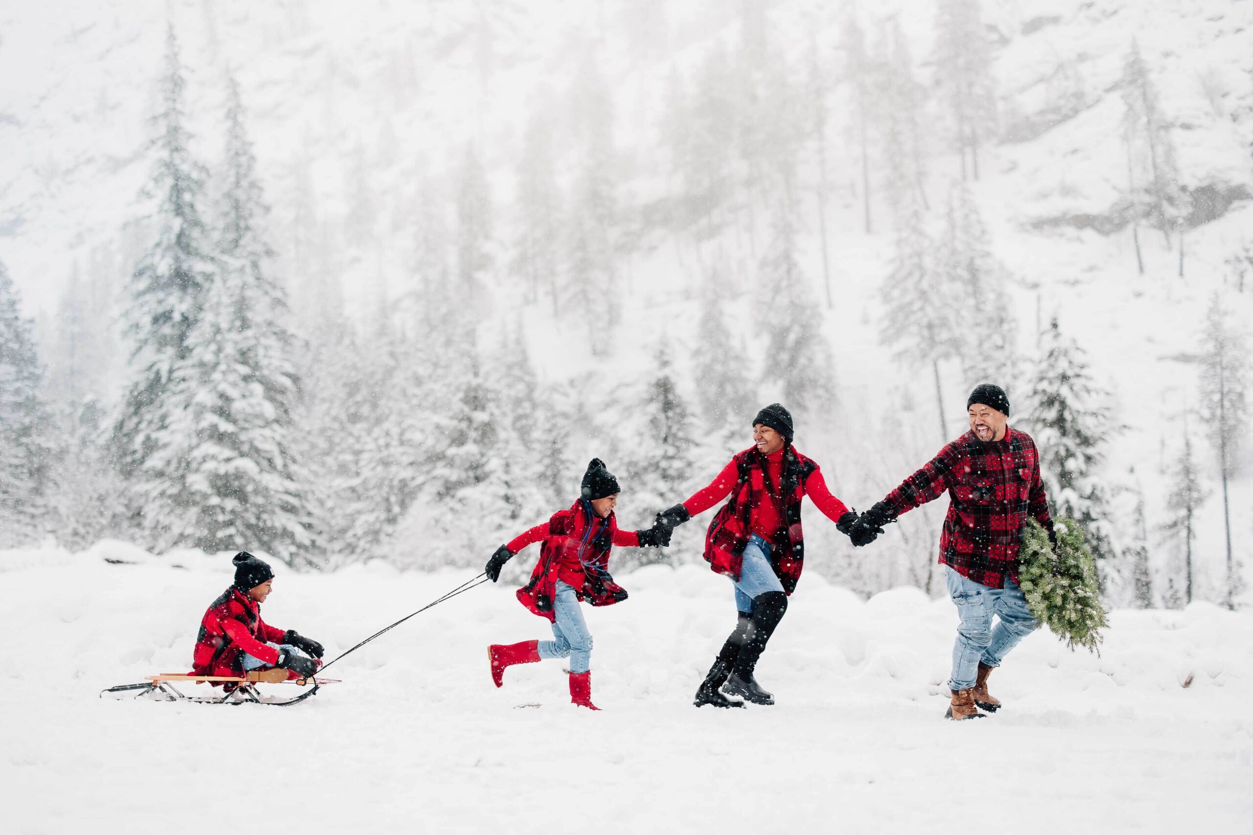 A mom and dad run in the snow pulling their youngest on a sled holding hands while enjoying things to do in leavenworth with kids in red plaid and jeans