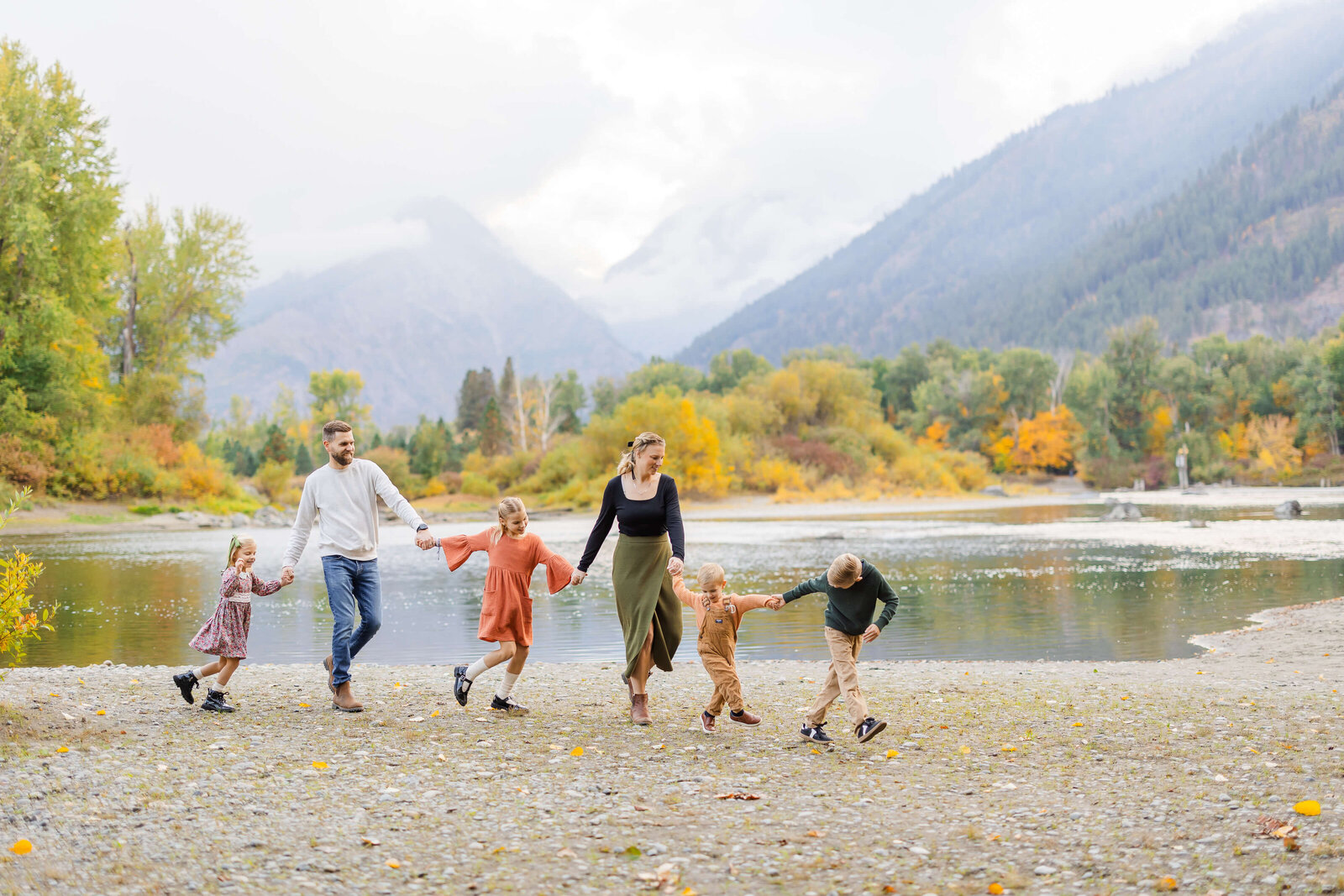 A young boy leads his parents and siblings by the hand along a river bank in the mountains while enjoying leavenworth autumn leaf festival