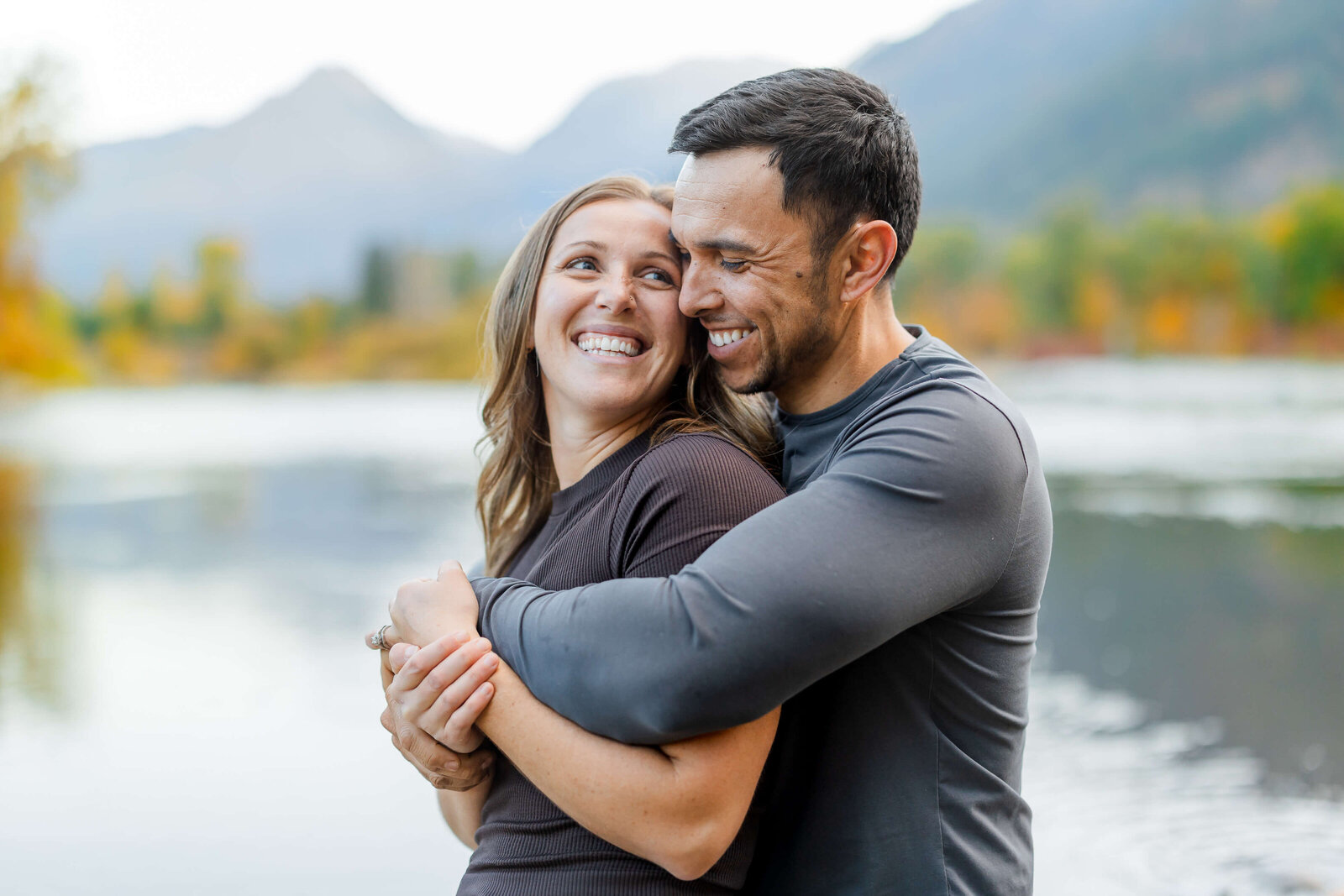 A happy couple snuggle on the edge of a river in grey at sunset in the mountains
