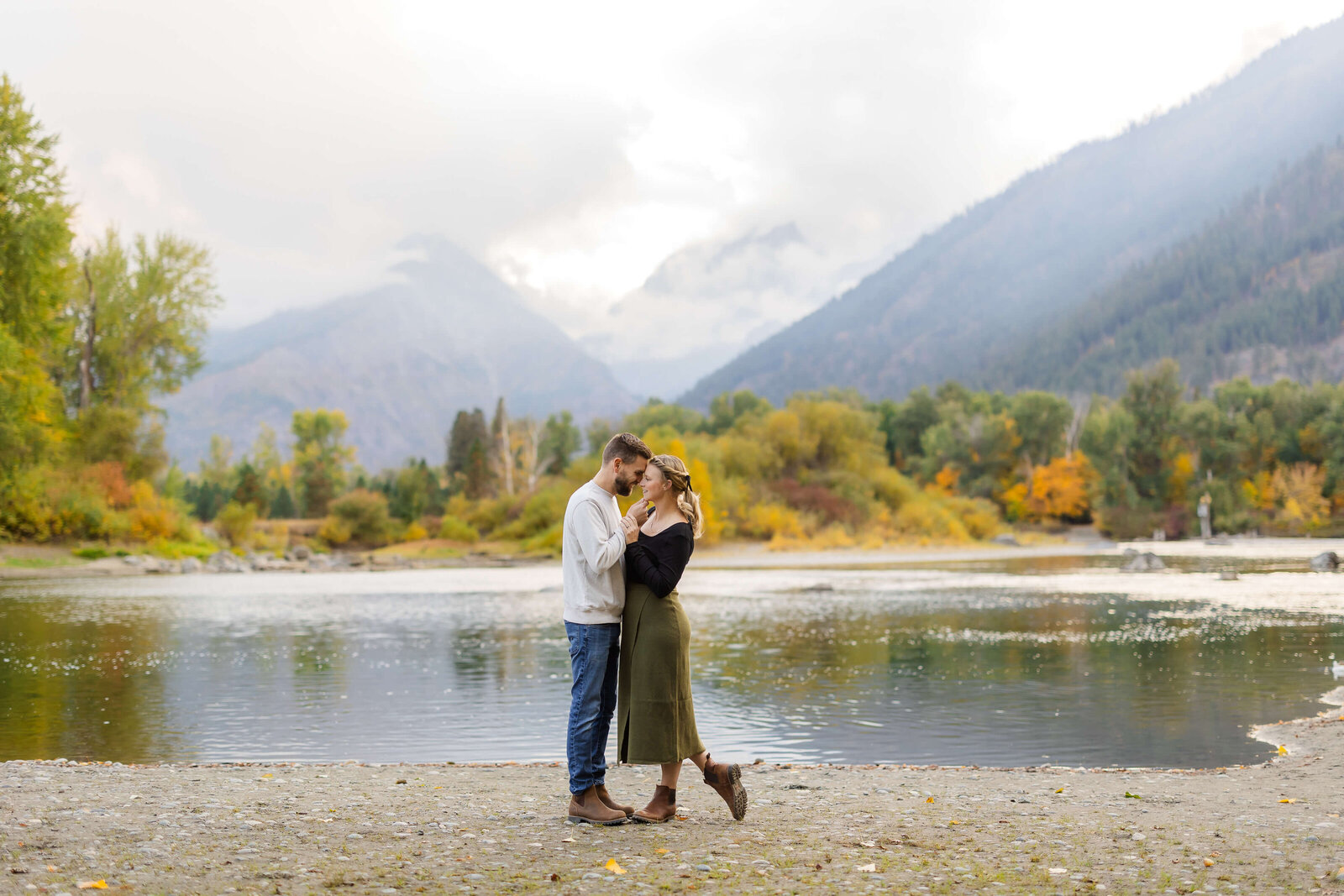 A happy couple dances along the river touching foreheads in the mountains at sunset before heading to leavenworth oktoberfest