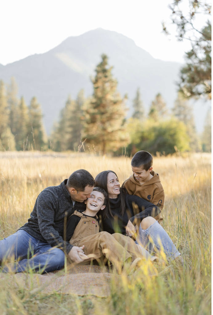 A mom and dad cuddle and giggle with their two young sons in a field of grass at sunset after exploring Leavenworth Oktoberfest
